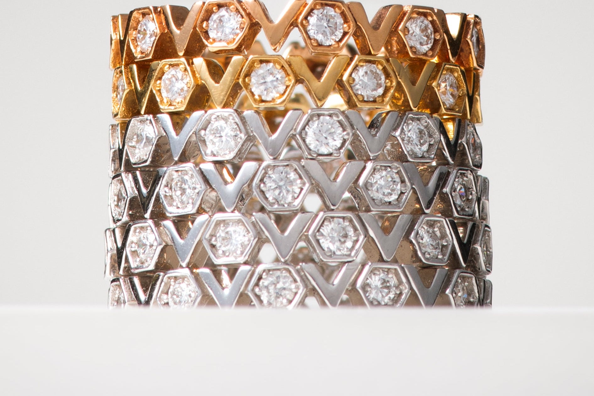 Two diamond-encrusted rings, one gold and one silver, on a light gray background.